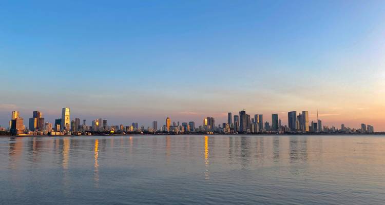 Vista panorámica del skyline moderno de Mumbai reflejando tonos dorados en las aguas tranquilas del atardecer.