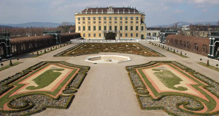 Jardins à la française menant à un grand bâtiment dans un complexe palatial.