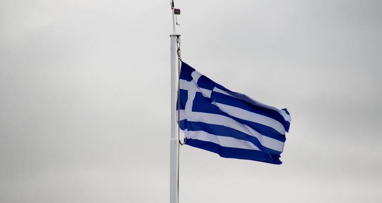 Greek flag waving on a pole against a cloudy sky.