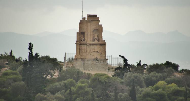 Monument surrounded by trees with hills in the background.