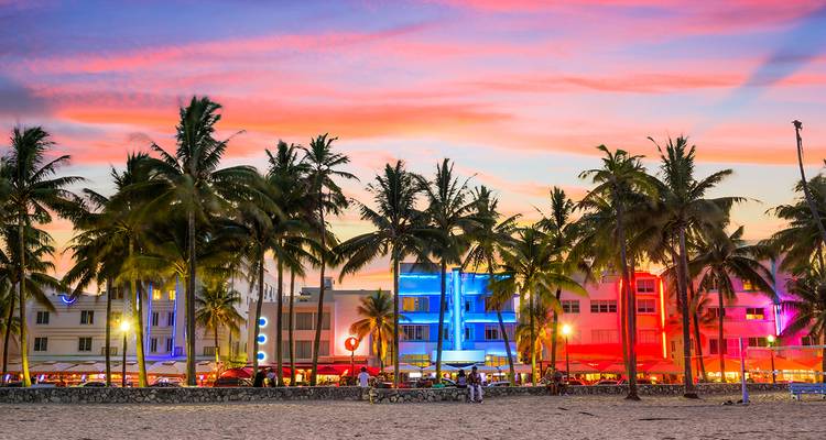 Beachfront with colorful buildings and palm trees at sunset.