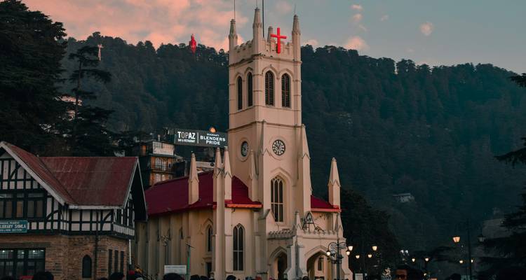 Gotische gele kerk met rood dak tegen met dennen bedekte heuvels bij zonsondergang.