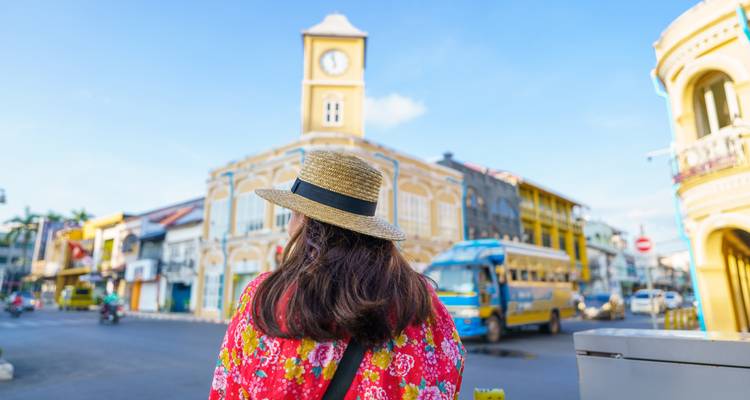 Back view of a person wearing a hat and floral attire looking at a clock tower.