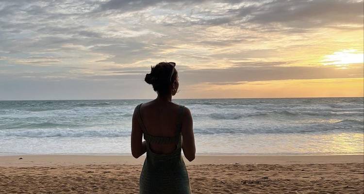 A person standing on the beach looking at the ocean during sunset.