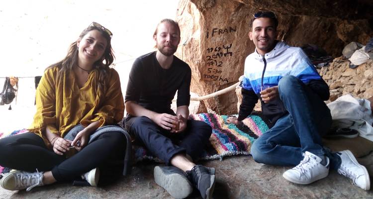 Three people relaxing inside a cave on colorful rugs.