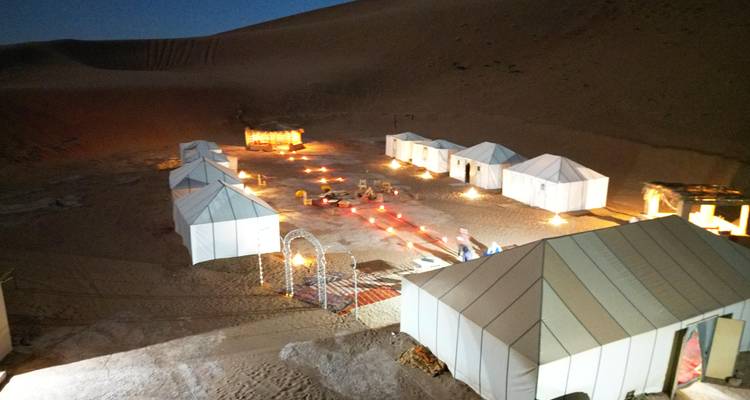 Vue nocturne d'un campement dans le désert avec des lumières scintillantes.