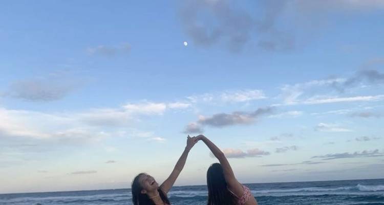 Two women playing in the ocean under a bright sky.