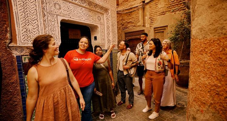 Grupo de turistas escuchando a la guía frente a la puerta ornamentada de un riad en la medina de Marrakech.