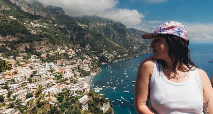 Une femme avec une casquette surplombant une ville côtière avec des bateaux dans l'eau.