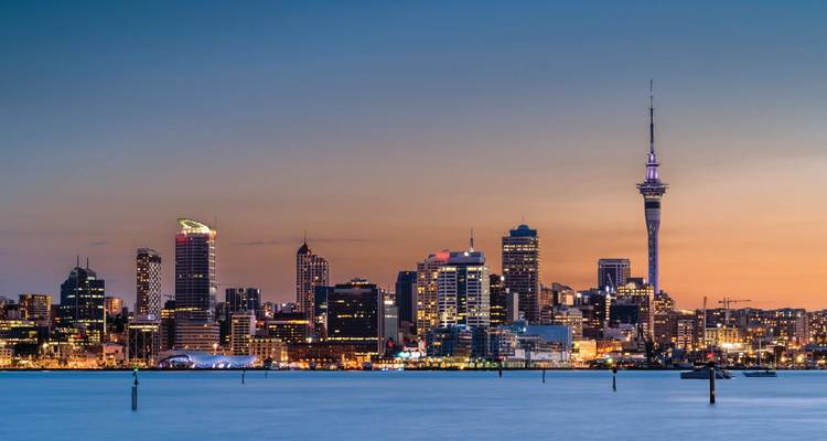 Skyline d'Auckland en soirée avec la Sky Tower qui s'élève au-dessus du port au crépuscule.