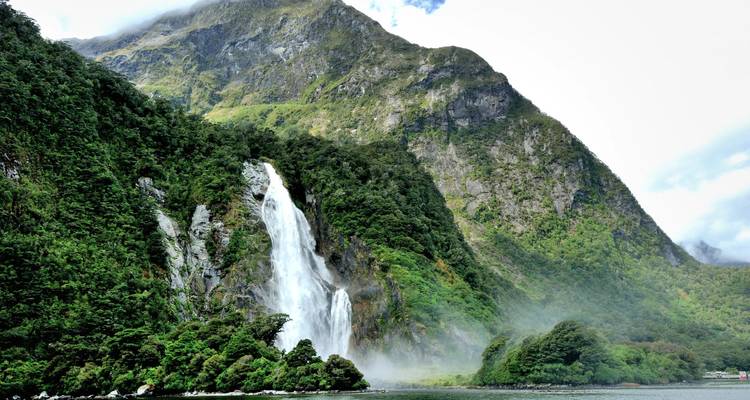 Une puissante cascade se jette des falaises verdoyantes dans le fjord brumeux de Milford Sound.