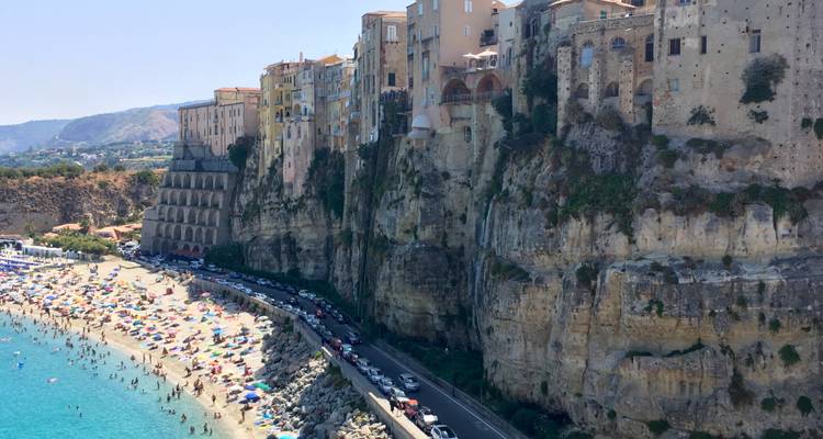 Une ville à flanc de falaise surplombant une plage avec des parasols et une route.