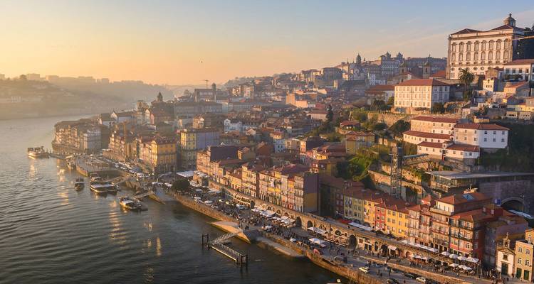 La lumière dorée du soir baigne les édifices colorés du bord de fleuve du quartier historique de Porto