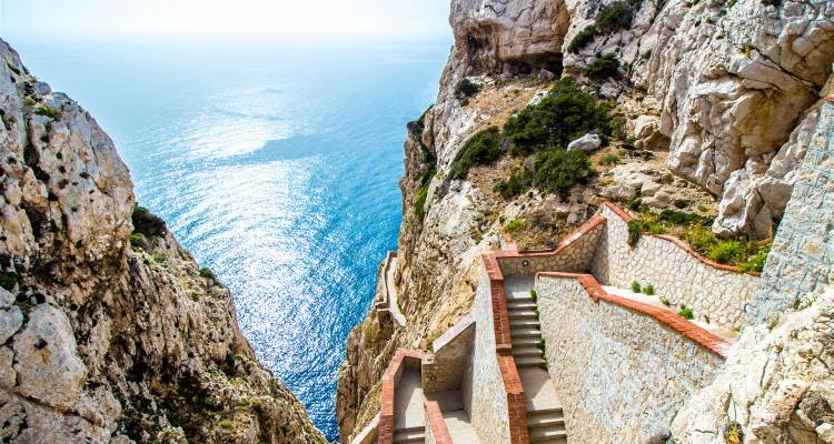 Escalier descendant une falaise vers la mer, avec une vue sur l'océan bleu.