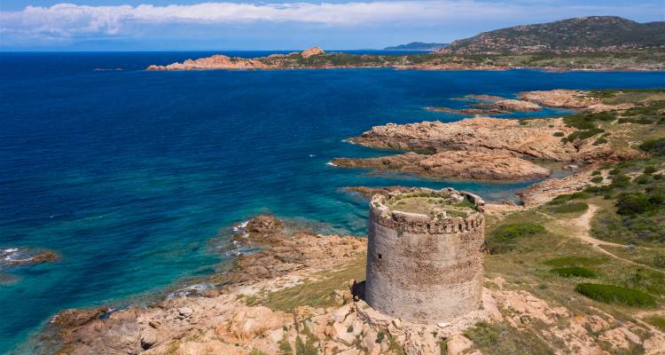 Ancienne tour de pierre sur un littoral avec une eau turquoise.