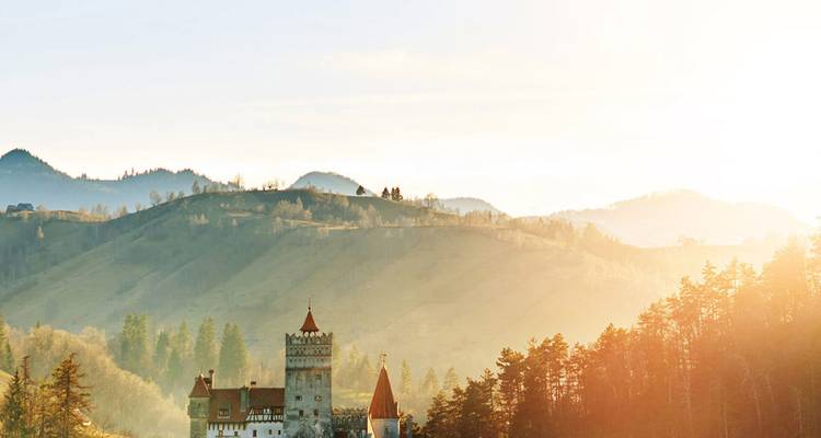 Märchenschloss eingebettet zwischen bewaldeten Hügeln unter warmem goldenem Sonnenlicht.