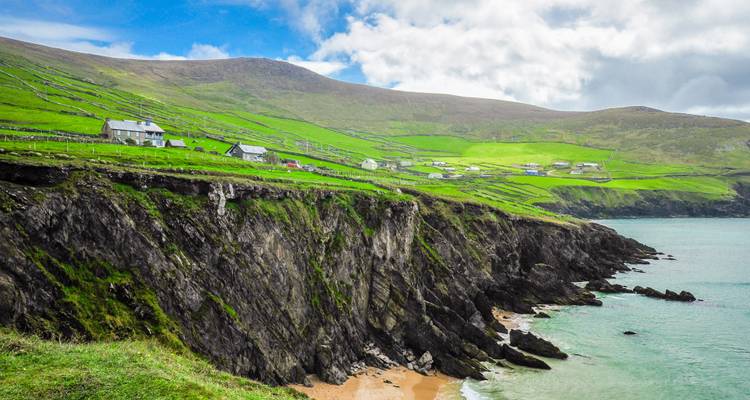 Lush green cliffs with small houses overlooking the sea.