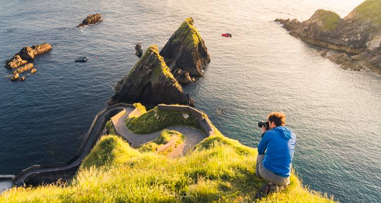 Photographer sitting atop a cliff capturing the shoreline.
