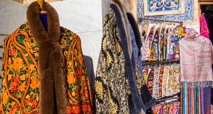 Manteaux ouzbeks brodés aux couleurs vives et textiles à motifs suspendus à un étal de bazar.