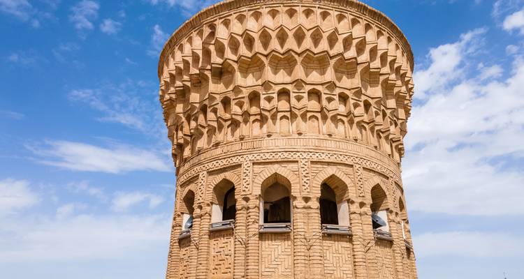 Minaret en brique sculpté de manière ornementale avec des arches décoratives se dressant contre un ciel bleu vif.