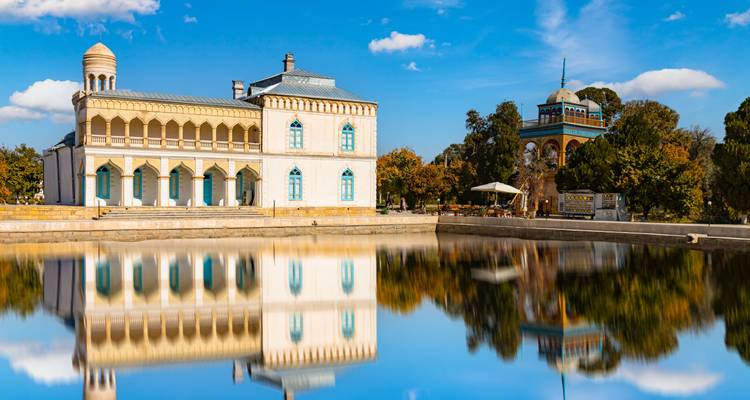 Piscine historique de Lyab-i Hauz reflétant un bâtiment blanc à colonnades et un pavillon sous un ciel bleu.