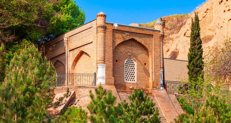 Petit mausolée en briques entouré de pins sur une colline ensoleillée.