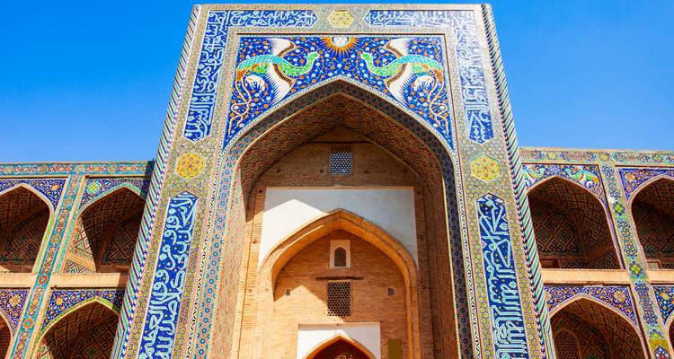 Grand portail voûté d'une médersa carrelée richement décorée de mosaïques bleues et jaunes.