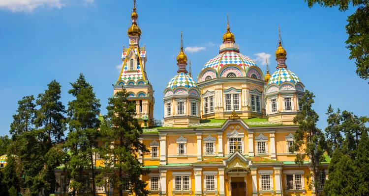 Kleurrijke Russisch-orthodoxe Zenkov-kathedraal omlijst door hoge dennenbomen onder een heldere blauwe hemel.