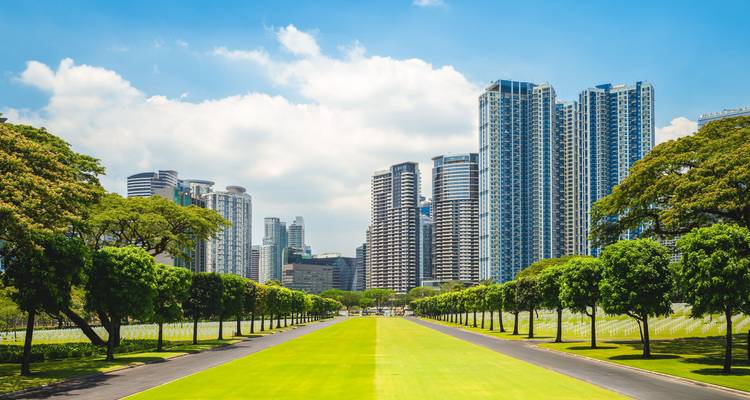 El moderno horizonte de Manila se alza más allá de un parque verde bien cuidado bordeado de árboles.