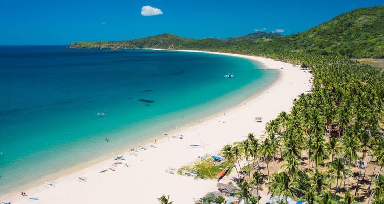 El mar turquesa acaricia una larga media luna de arena blanca como polvo bordeada de palmeras.