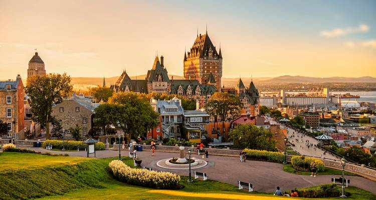 Panoramisch uitzicht op Quebec City tijdens het gouden uur met het iconische Château Frontenac dat uitkijkt over de St. Lawrence rivier, historische gebouwen en mensen die door het park wandelen.