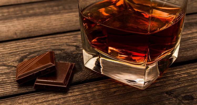 Glass of whiskey with chocolate on a wooden surface.