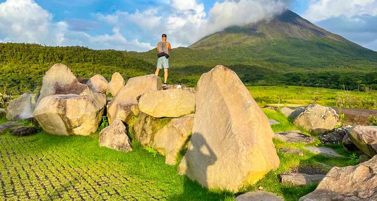 Randonneur debout sur des rochers avec le volcan Arenal en arrière-plan.