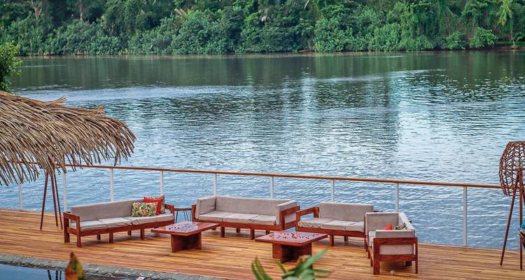 Außensitzbereich neben einem ruhigen Fluss, umgeben von Dschungel.