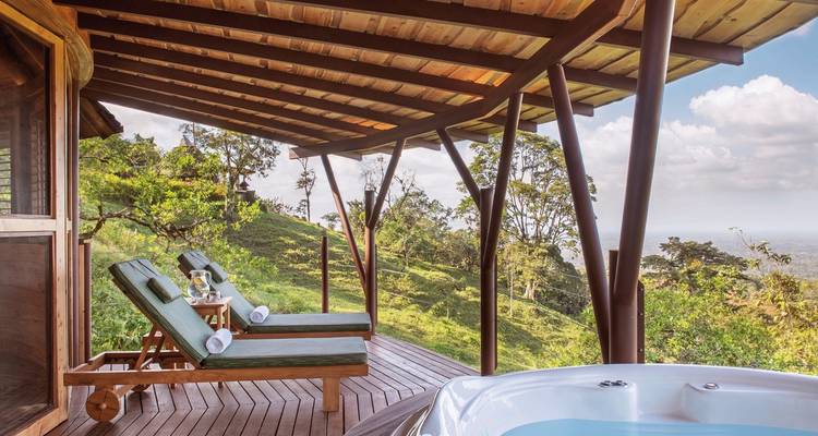 Wooden terrace with loungers and a hot tub overlooking hills.