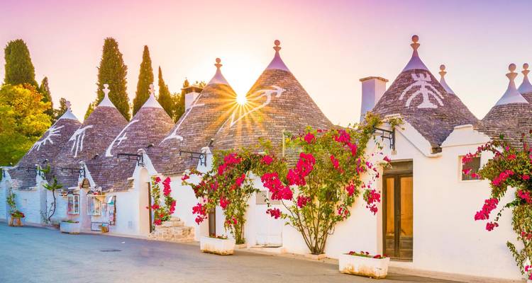Trulli-huizen met bloemen onder een kleurrijke hemel.