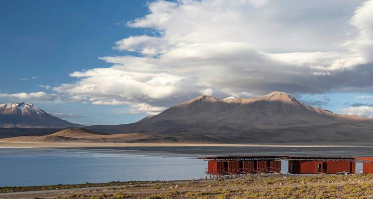 Ein malerischer Blick auf einen See mit Bergen im Hintergrund und einem Bauwerk am Ufer.