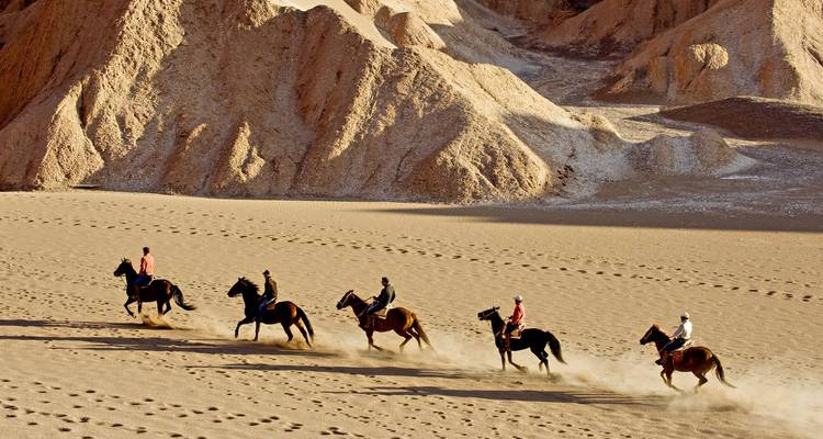 Menschen reiten auf Pferden durch eine Wüstenlandschaft.