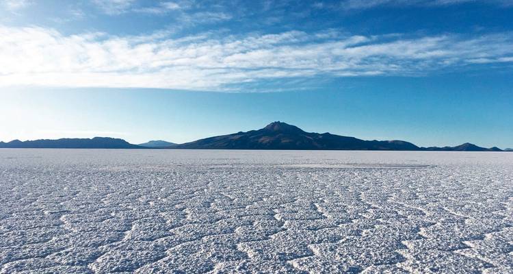 Eine weite Salzebene mit einem fernen Berg unter blauem Himmel.