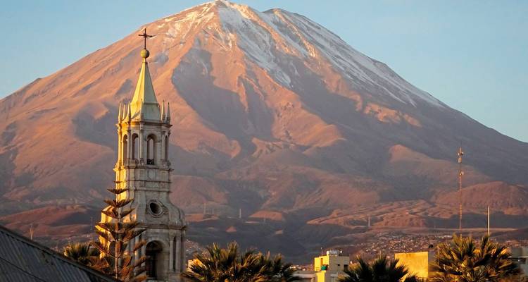 Une tour d'église avec une montagne enneigée en arrière-plan.