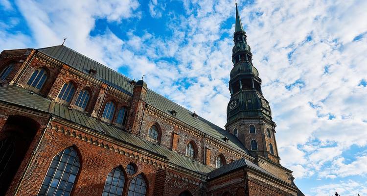 Large church with a tall spire under blue sky in Riga.