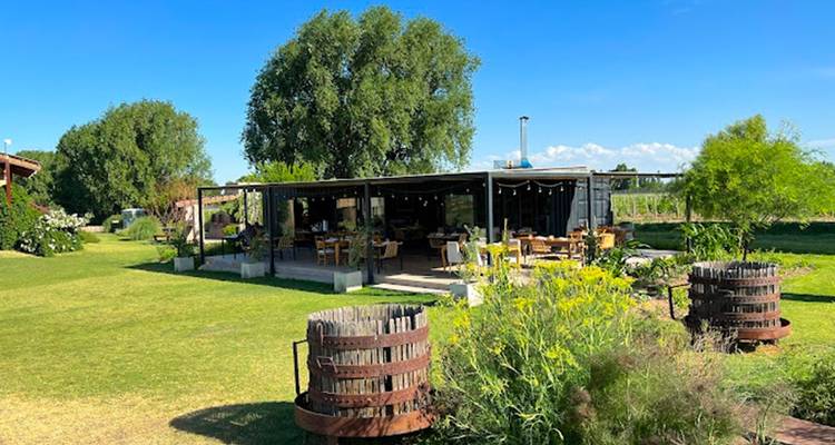Espace de restauration en plein air avec des tables sous une pergola entourée d'herbe et d'arbres.
