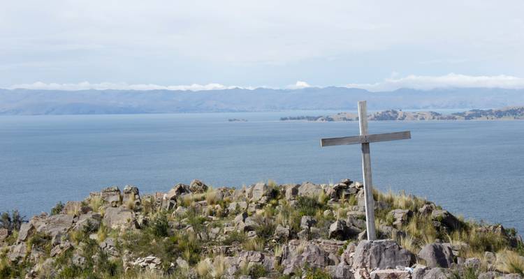 Croix sur une colline rocheuse surplombant un lac.
