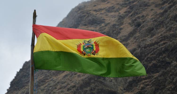 Drapeau bolivien flottant devant un paysage montagneux.