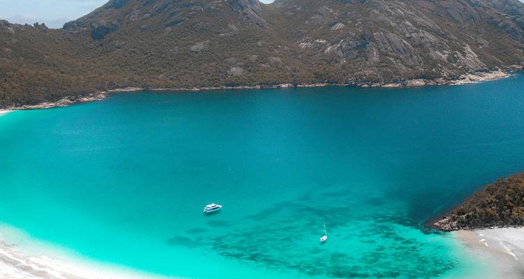 Vue aérienne d'une baie turquoise avec un bateau et une plage de sable.