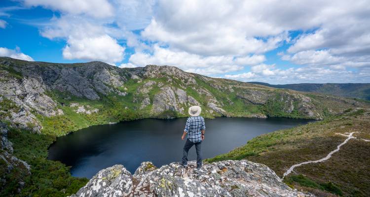 Persona parada en un acantilado rocoso con vista a un lago.