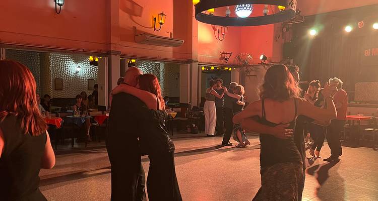 Les couples dansent le tango dans une salle de milonga chaleureusement éclairée avec de petites tables et une décoration rouge.