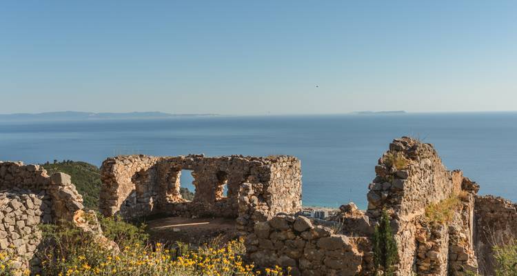 Ruines d'une forteresse de pierre perchée sur une falaise côtière surplombant la mer Ionienne bleu calme.