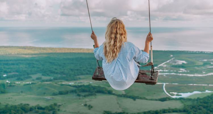 Woman swinging over a valley with the ocean in the distance.