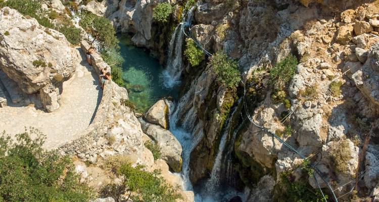 Waterfall in rocky terrain with a person on a path.